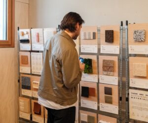 Visitor examining material samples mounted on timber boards while holding a drink.
