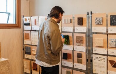 Visitor examining material samples mounted on timber boards while holding a drink.