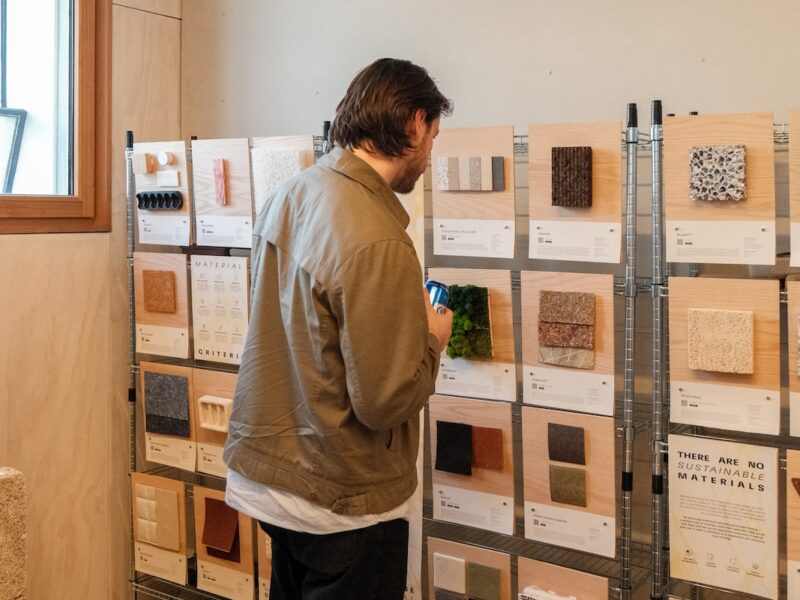 Visitor examining material samples mounted on timber boards while holding a drink.