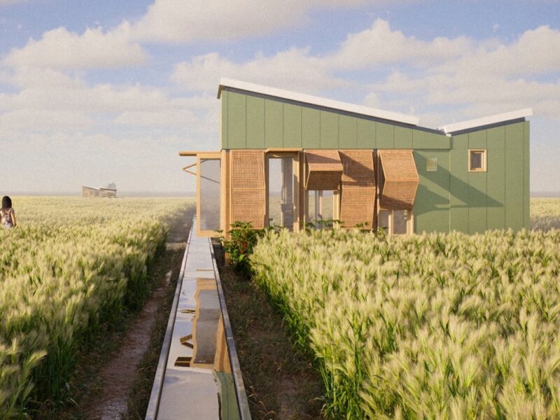 A small prefabricated house elevated above agricultural fields, with rainwater channels leading toward the structure and vegetation surrounding the site.