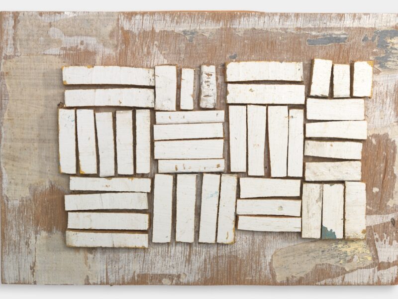 Assemblage of rectangular white-painted wooden fragments arranged in blocks on a weathered timber backing.