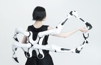 Person wearing a white multi-jointed robotic exoskeleton with articulated arms extending outward.