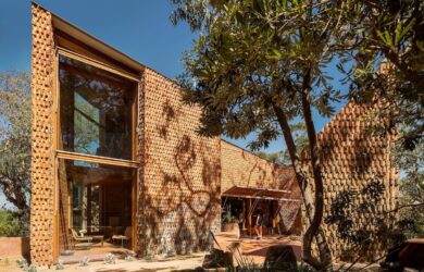 House clad in handcrafted terracotta tiles with deep window openings set within a coastal landscape.